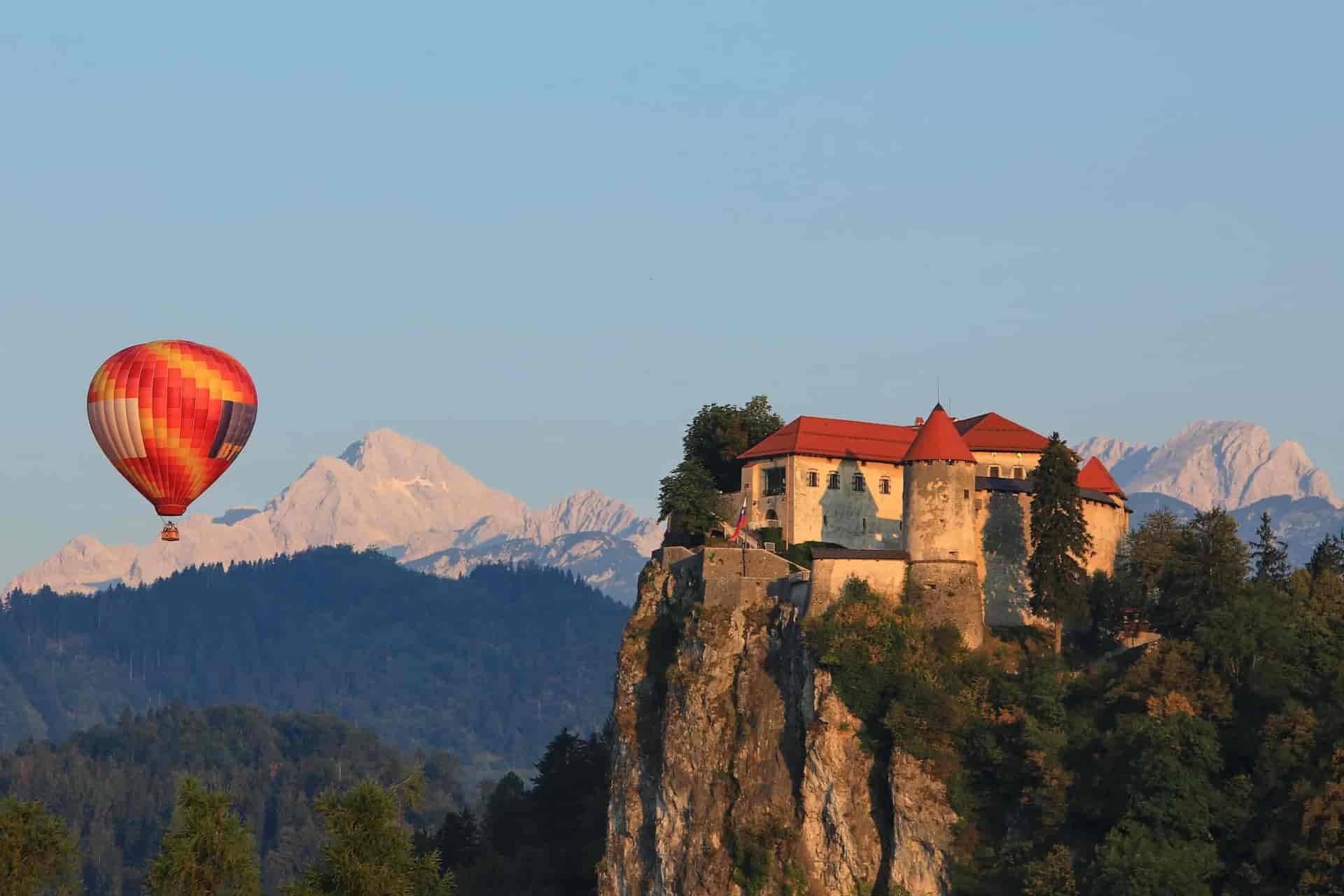Hot air balloon flying near castle on cliff with snowy mountains in background