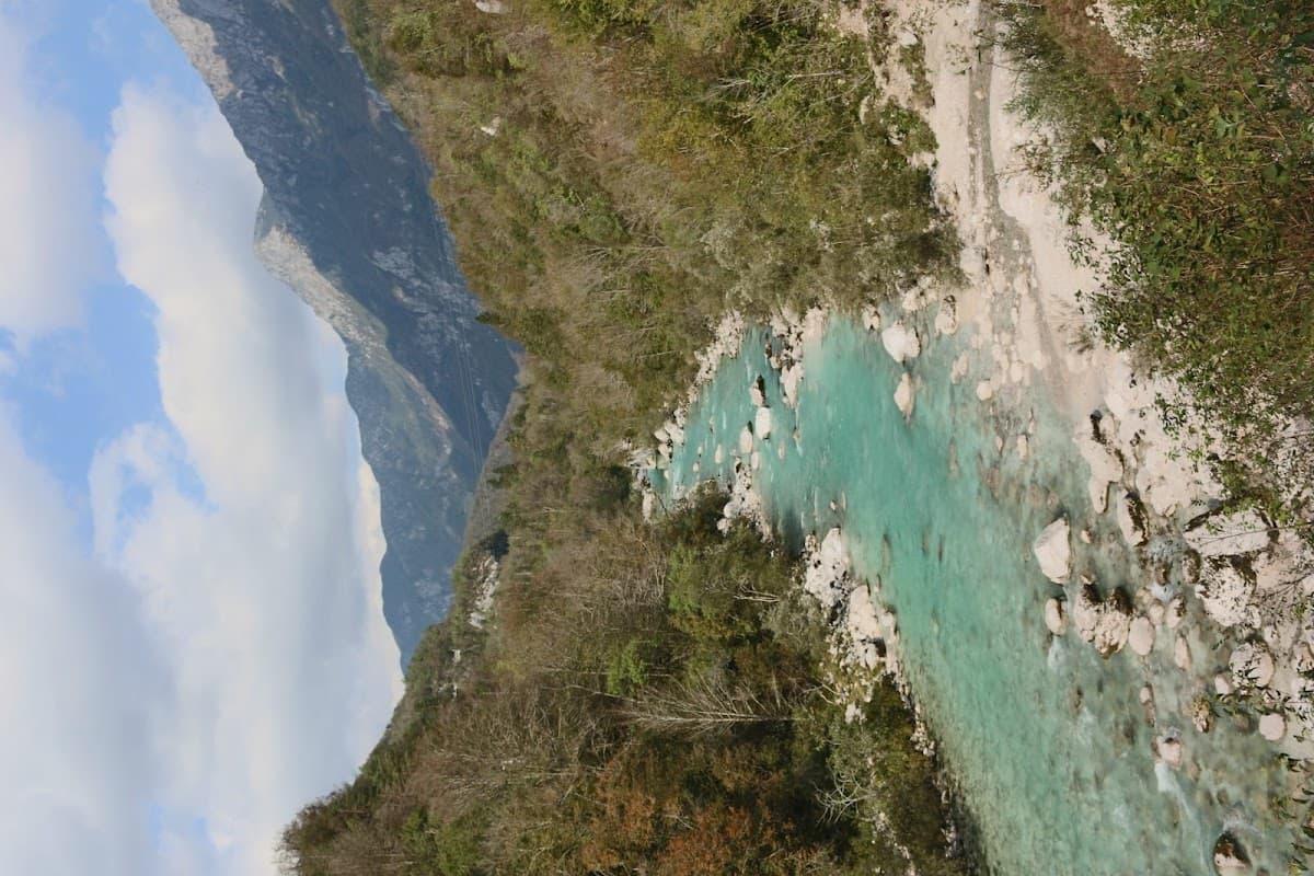 Turquoise river flowing through a rocky gorge with steep, forested mountains under a cloudy sky.