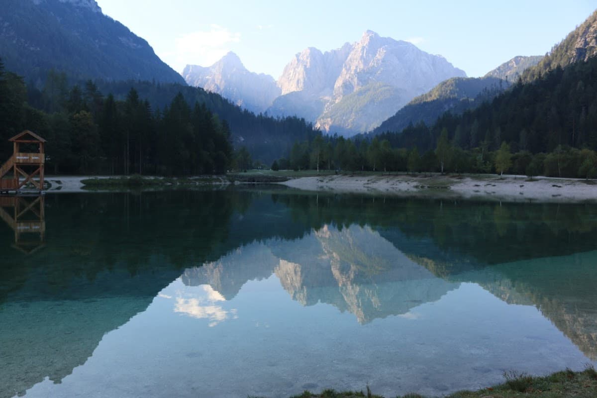 Mountain peaks reflected in clear lake water with a wooden observation tower on the shore