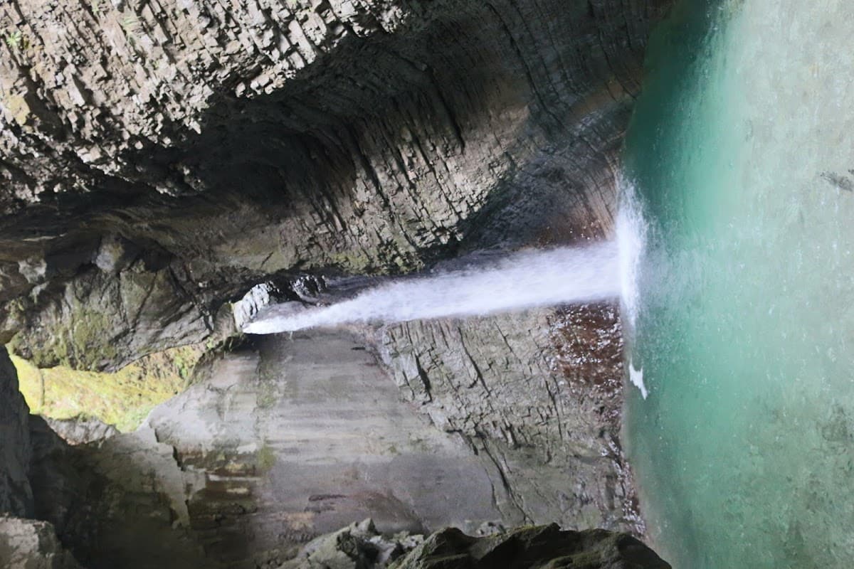 Waterfall plunging into turquoise pool inside a rocky cavern or gorge