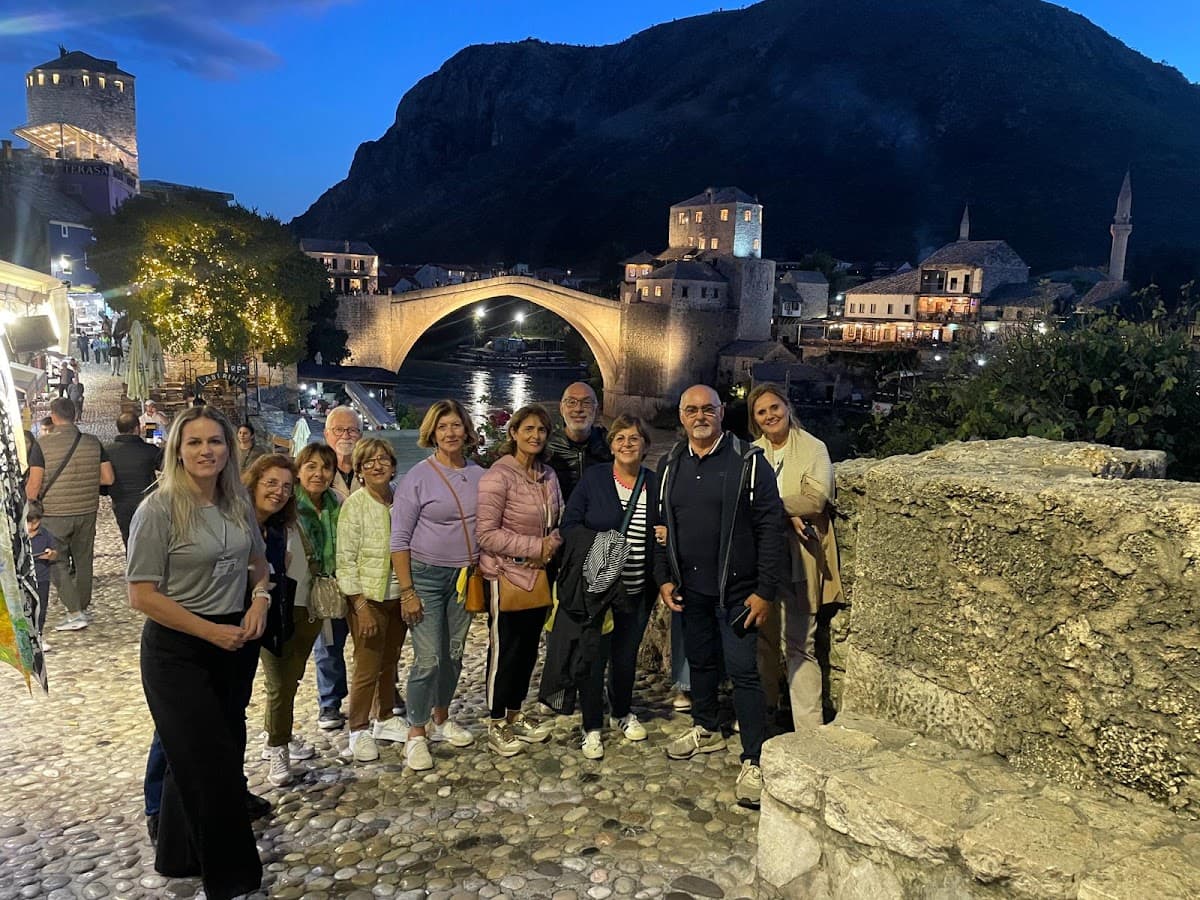 Group posing on cobblestones near Stari Most bridge at dusk in Mostar, Bosnia and Herzegovina.