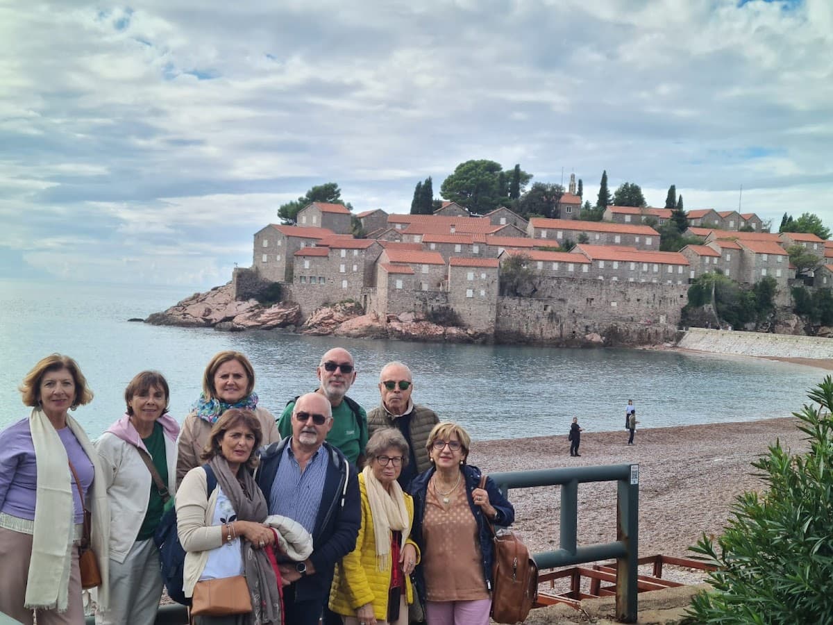 Group posing before Sveti Stefan island resort with stone buildings and terracotta roofs