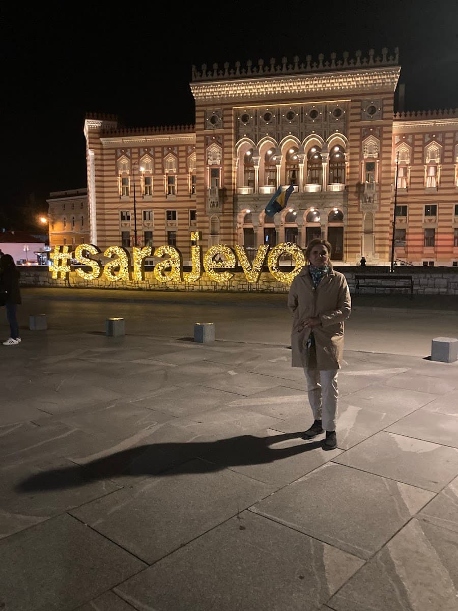Woman standing by illuminated #Sarajevo sign in front of historic building at night