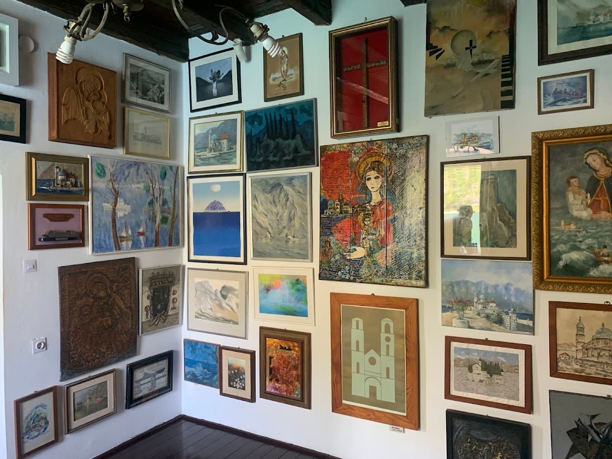 Gallery corner with numerous framed paintings and religious art hanging on white walls.