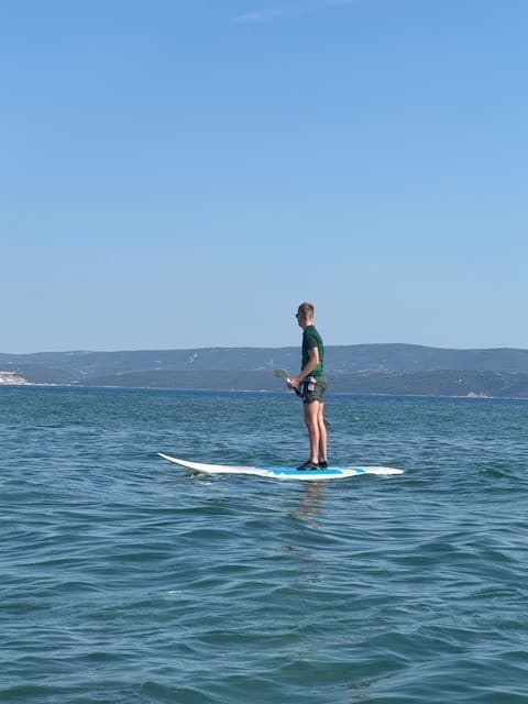 Man stand-up paddleboarding on wavy blue sea with distant mountains under clear sky