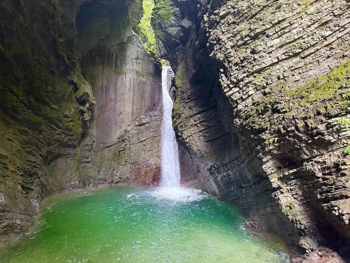Waterfall plunging into a bright green pool in a narrow, moss-covered rock canyon
