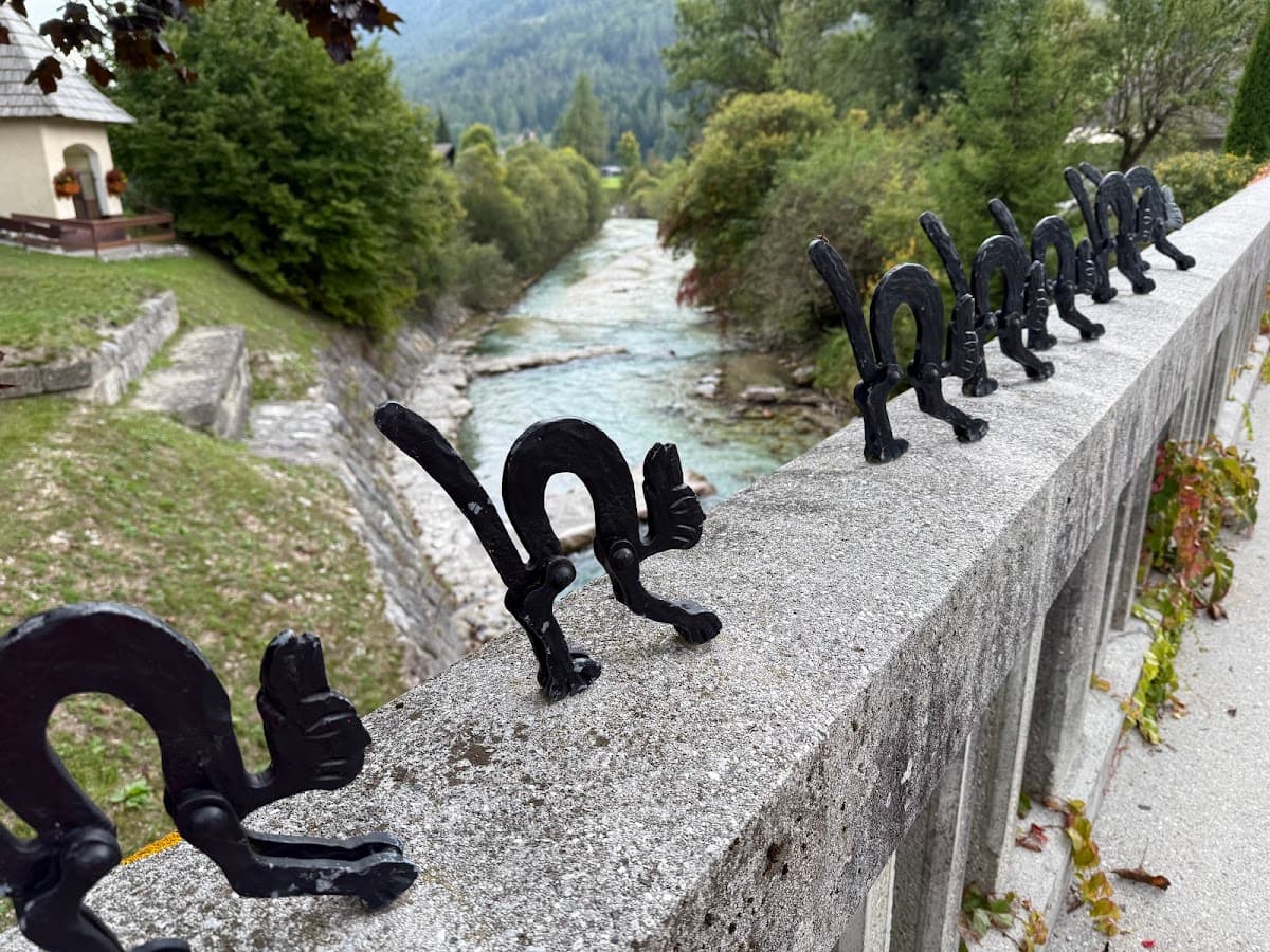 Black metal cat figures on bridge railing above a river in a green valley setting.