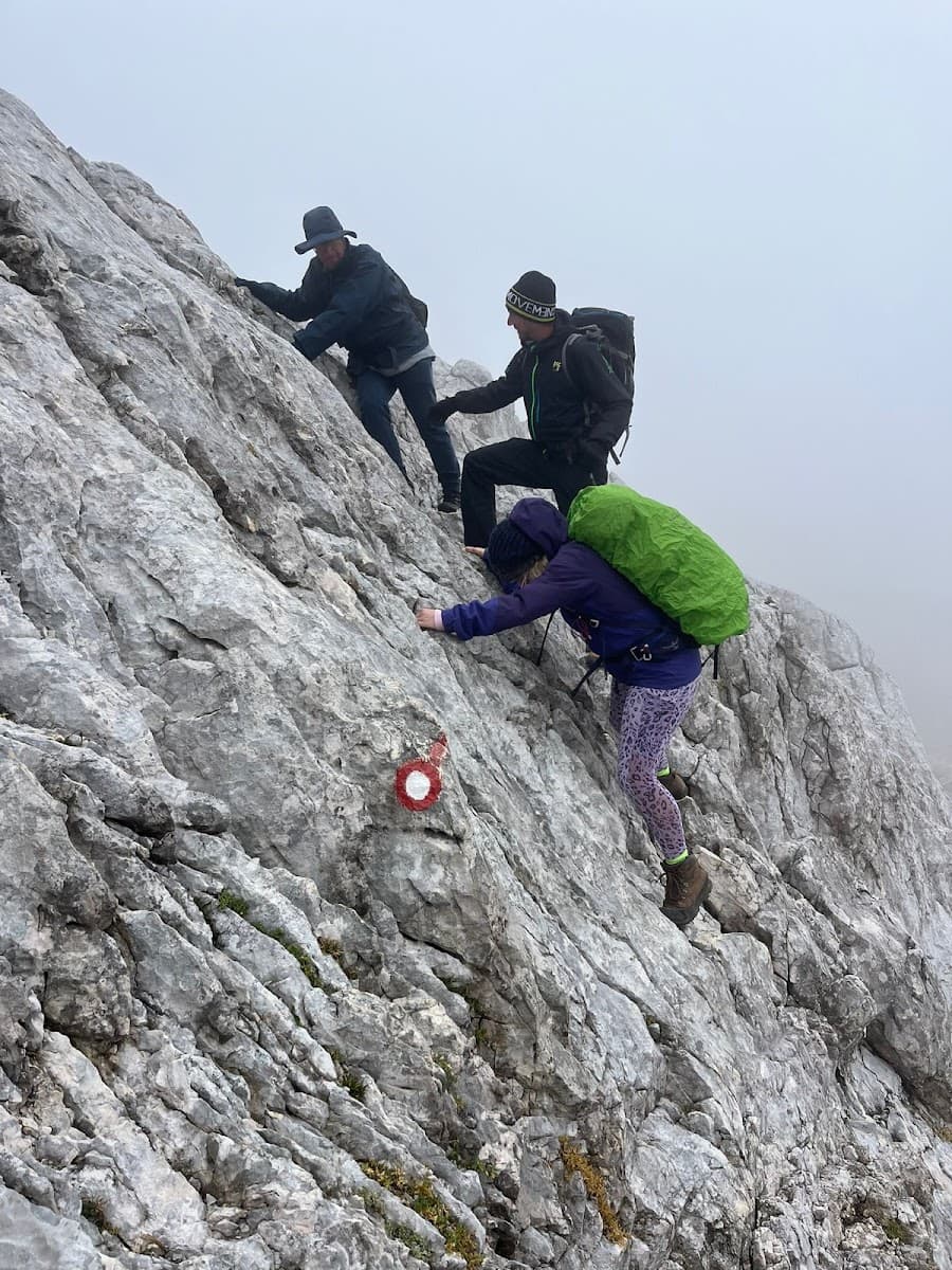 Hikers ascending steep, rocky terrain marked with a red and white trail blaze in fog.