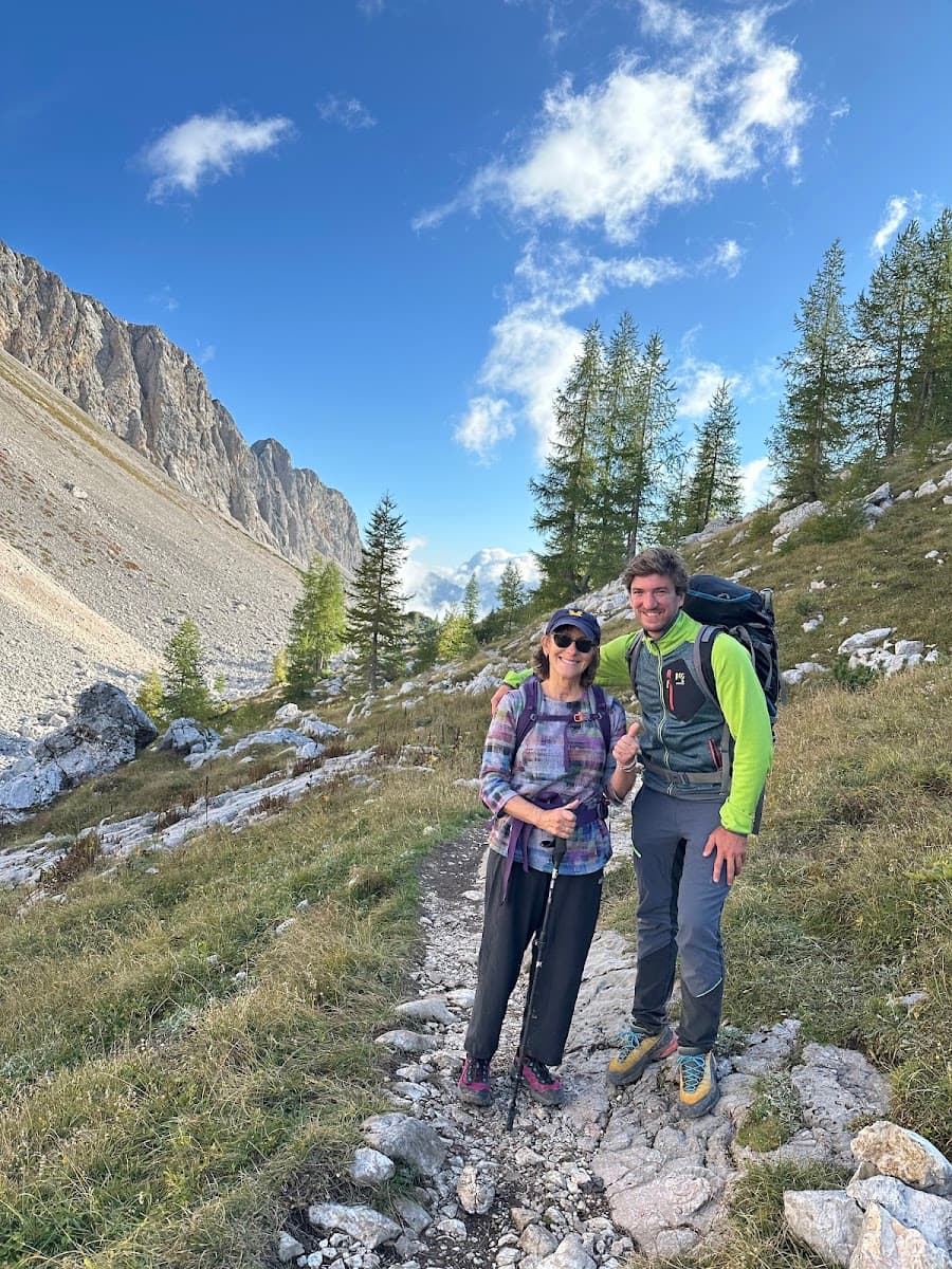 Two hikers with backpacks and poles on rocky mountain trail under blue sky