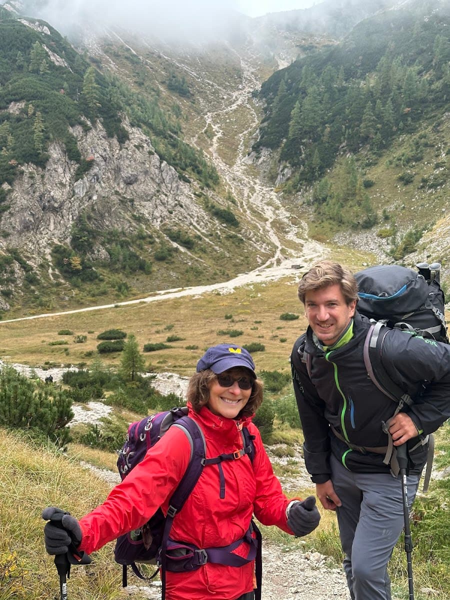 Hikers with backpacks and trekking poles on trail in steep, foggy mountain valley