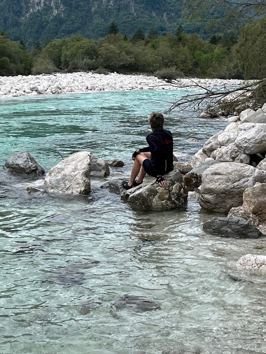 Person sitting on a rock by a turquoise river with forested banks