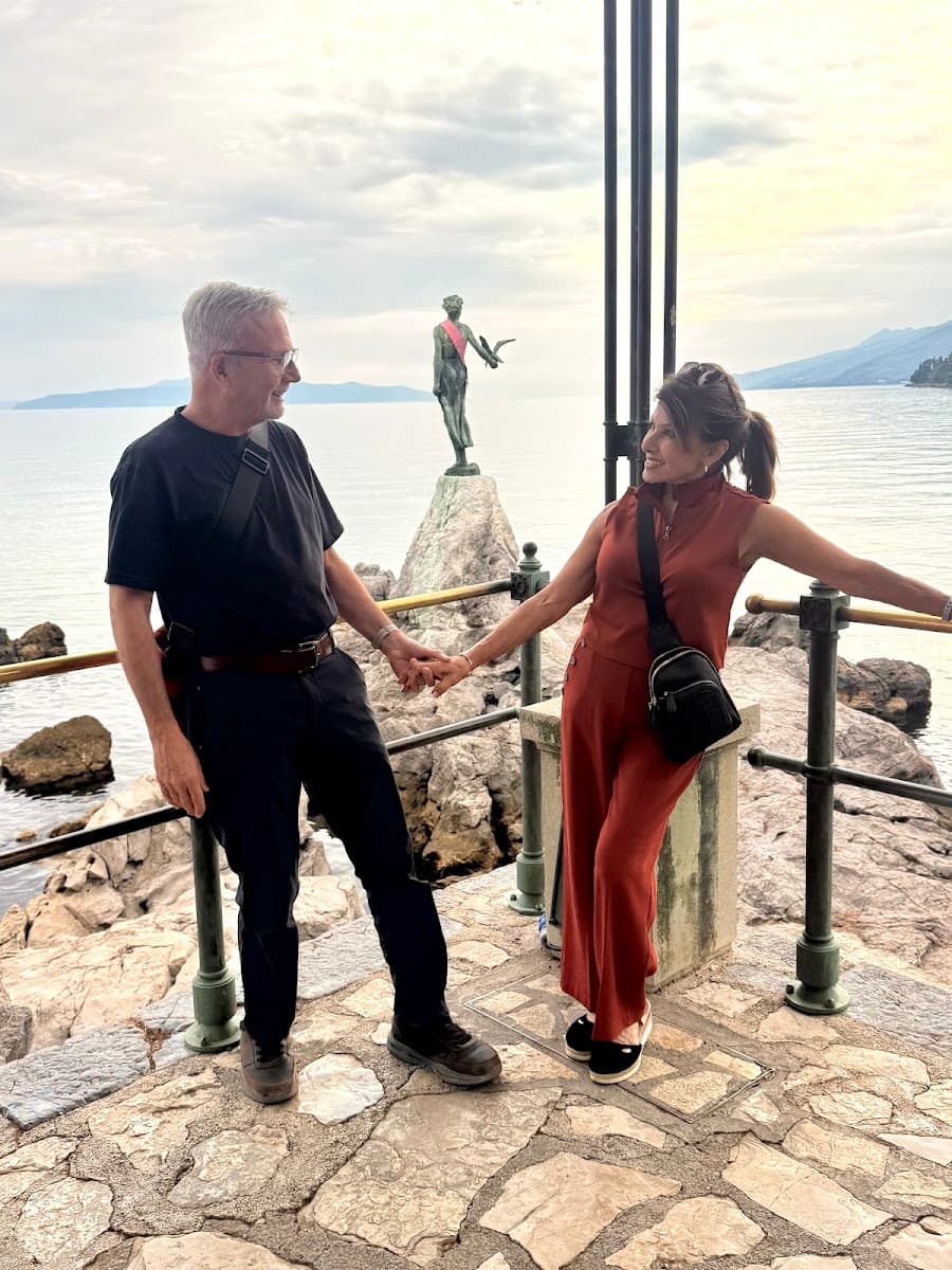 Couple holding hands on coastal terrace near statue and sea view