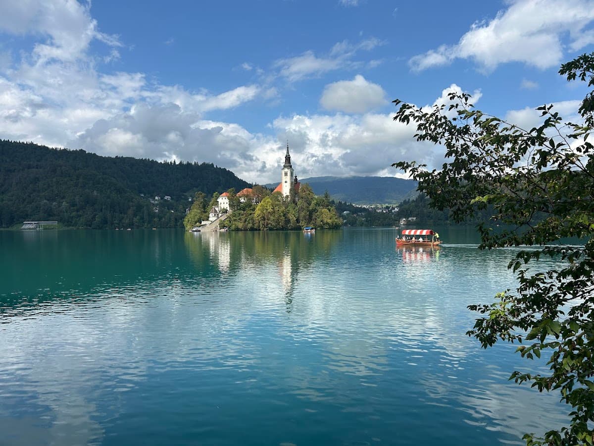 Pletna boat on Lake Bled with island church and forested hills under blue sky.