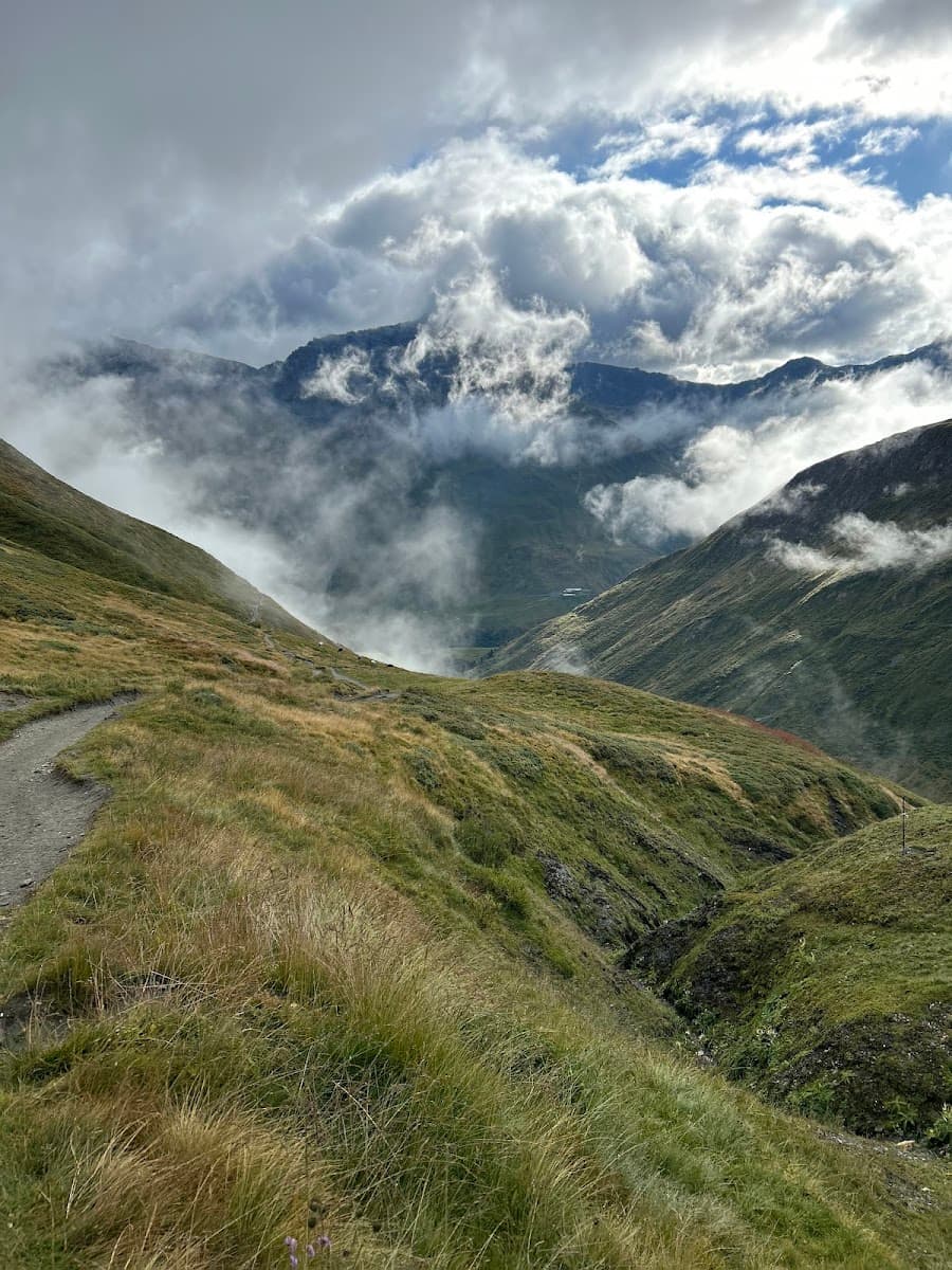 Hiking trail on grassy mountain slope with peaks shrouded in low clouds