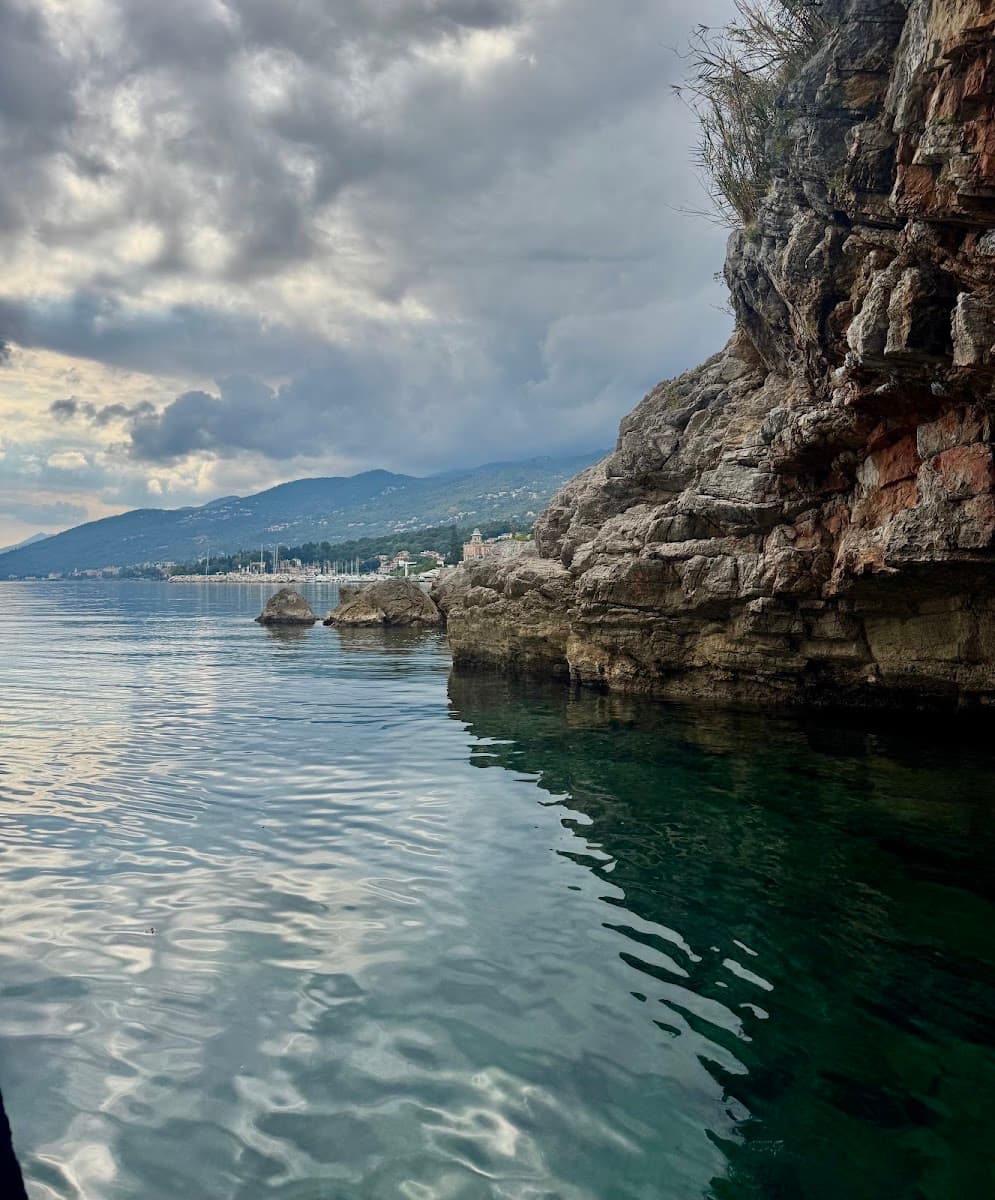 Rocky coastline and calm sea under cloudy skies with distant mountains